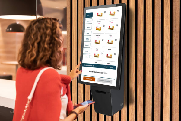 A girl orders food and lunch at a fast food restaurant using a self-service kiosk or a terminal with a screen. Modern commerce equipment