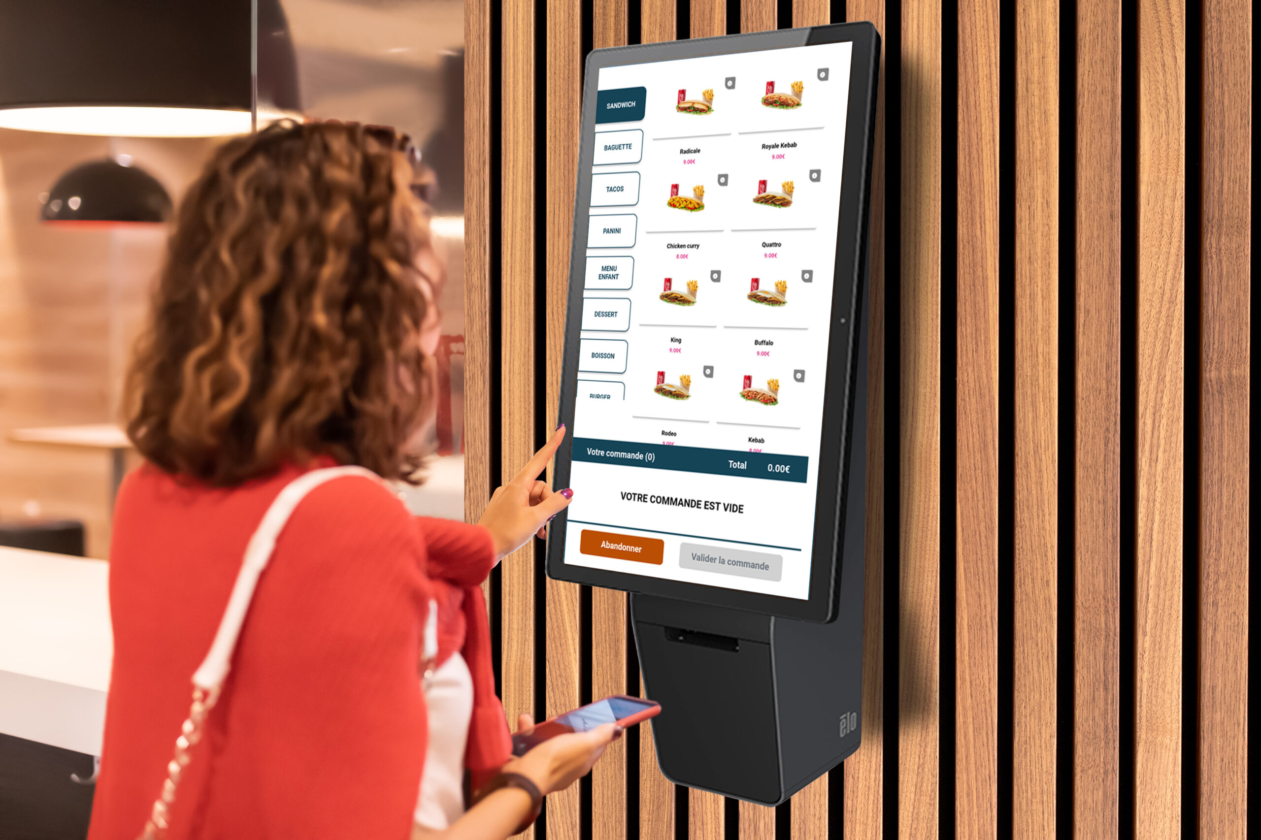 A girl orders food and lunch at a fast food restaurant using a self-service kiosk or a terminal with a screen. Modern commerce equipment